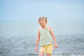 Blonde girl standing on the beach and looking at the camera with the sea in the background on a cloudy summer day