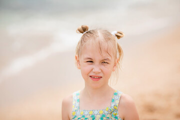 Close-up portrait of a smiling girl with pigtails and windblown hair on a cloudy beach day
