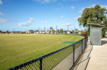 Open sports field with well-maintained green grass lawn, bordered by a chain-link fence with a shelter. Community recreational space for local sporting activities in Tarneit, Australia