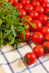 Red ripe cherry tomatoes and fresh spicy rocket salad on white checked towel, focus on foreground