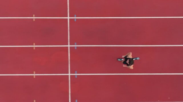 Aerial top view of a solo male athlete sprinting along a marked track lane, showcasing the track boundaries, emphasizing speed, focus, and precision in motion. Cinematic drone slow motion