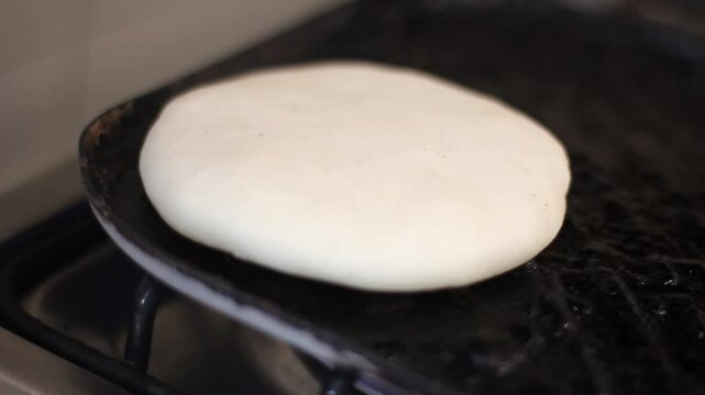 Turning the corn cake or arepa over the hot surface of the cast iron pan or budare.