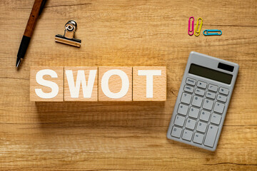There is wood cube with the word SWOT. It is an abbreviation for strengths, weaknesses,...