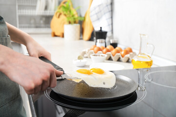 Woman taking fried eggs from frying pan in kitchen, closeup