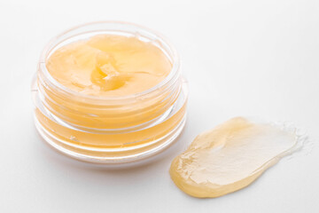 Jar and sample of lip balm on white background, closeup