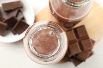 Tasty chocolate milk and pieces on white table, flat lay