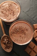 Tasty chocolate milk with shavings and pieces on black table, flat lay