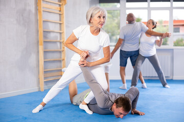 Fototapeta premium Sportive aged lady practicing arm twist technique against her partner during self-defense courses