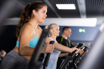 Fototapeta premium Active young woman training at elliptical machine in gym