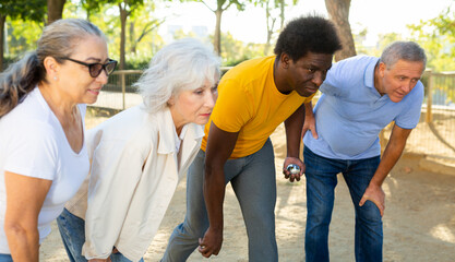 Obraz premium Happy casual, diverse pensioners exercising together petanque in fresh air in a sunny park in Spain