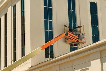 Construction lift, specifically a boom lift articulating being used for facade access on a building. Long extendable arm allows workers to reach elevated areas. Basket platform at the end of the boom 