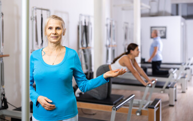 Fototapeta premium Portrait of mature female in sportswear smiling at camera while standing in Pilates rehabilitation center