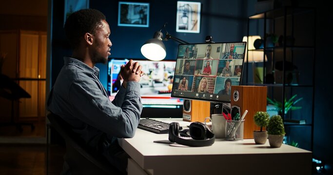 Colleagues attending a virtual webinar on pc from their homes, using a laptop for an online meeting call. Young african american man engrossed in the discussion, video conferencing. Camera A.