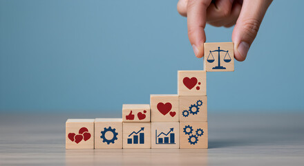 Hand Placing Balance Icon Atop Wooden Block Tower Symbolizing Business Ethics