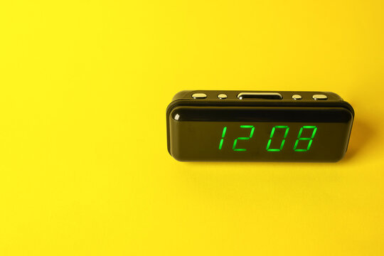 Digital alarm clock showing 12:08 o'clock on yellow background, space for text