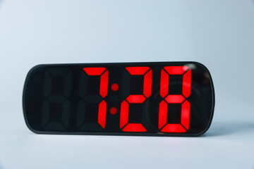 Digital alarm clock showing 7:28 o'clock on grey background, closeup