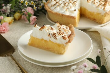 Piece of delicious pie with browned meringue and flowers on light textured table, closeup