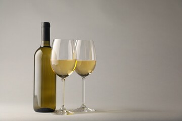 Tasty white wine in glasses and bottle on light grey background, space for text