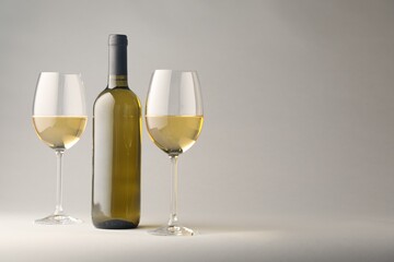 Tasty white wine in glasses and bottle on light grey background, space for text