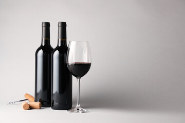 Tasty red wine in glass, bottles, corks and corkscrew on light grey background, space for text