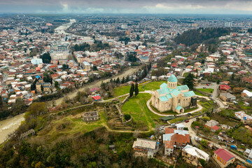 Aerial view of old neighborhoods of Kutaisi located along Rioni river overlooking restored medieval Orthodox Bagrati Cathedral on Ukmerioni hill in springtime, Georgia