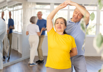 Positive senior man dancing playful Latin dance bachata with female partner during group class in...
