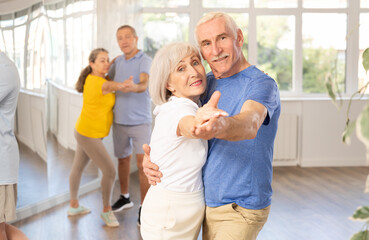 Obraz premium Smiling senior woman and man dancing slow ballroom dance during group class in choreography studio