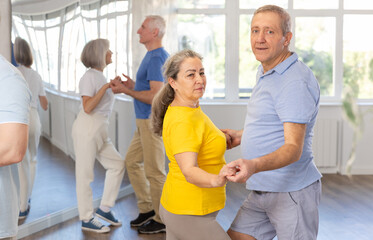 Obraz premium Cheerful senior woman practicing passionate samba with interested attentive man in dance class for adults. Amateur dancing concept..
