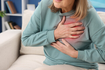 Fototapeta premium Heart attack. Senior woman suffering from pain in chest on sofa at home, closeup