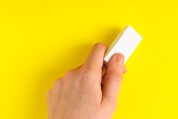 Woman using eraser on yellow background, closeup