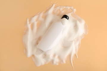 Bottle of cosmetic product with foam on beige background, top view