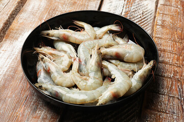 Fresh raw shrimps in bowl on wooden table, closeup