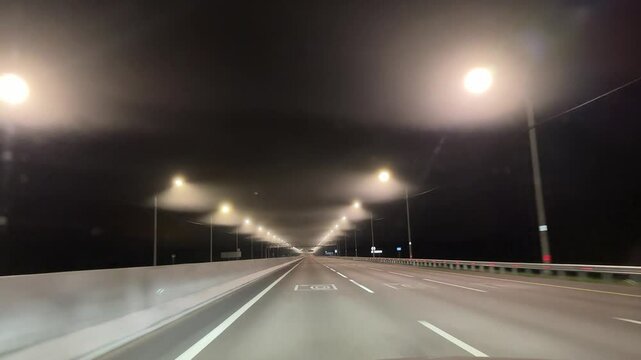 The highway is empty and dark, with only a few street lights illuminating the road. The sky is cloudy, and the air is cool and crisp. Scene is serene and tranquil