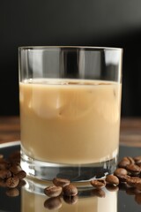 Coffee cream liqueur in glass and beans on table, closeup