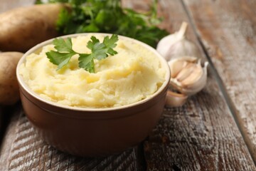 Delicious mashed potato with parsley and garlic on wooden table, closeup. Space for text