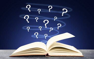 Question marks flying out from open book on grey table against dark blue background