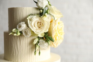Delicious wedding cake decorated with flowers on blurred white background, closeup