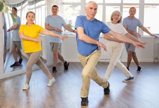 Expressive cheerful gentleman participating in upbeat Zumba class for group of seniors in mirrored fitness studio