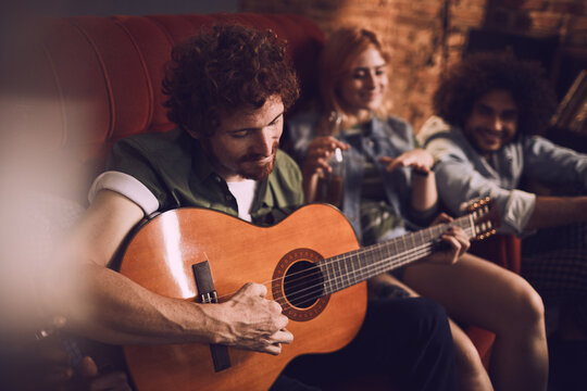 Young group of people playing the guitar and singing on a couch