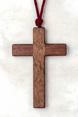 Dark wood cross pendant on maroon cord against marble