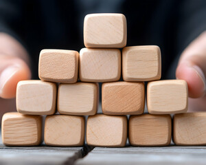 Hands carefully supporting a pyramid structure of light-brown wooden blocks