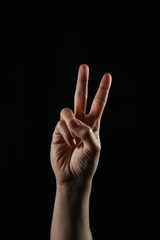 Close-up of a human hand showing a two-finger gesture, symbolizing peace or victory, on a black background. A popular sign in communication and culture.