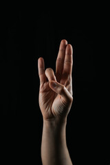 Close-up of a hand making a unique finger gesture on a black background. Symbolic or expressive sign, ideal for communication, creativity, or cultural context concepts.