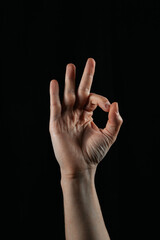 Hand showing OK gesture on black background. Symbol of approval, agreement, satisfaction, and positivity. Simple and powerful body language.