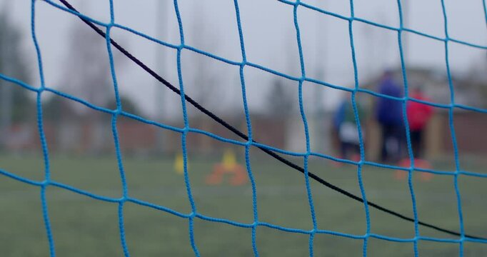 blue net on football goal to catch the ball after a kick, sports net for training, coach in the background in bokeh