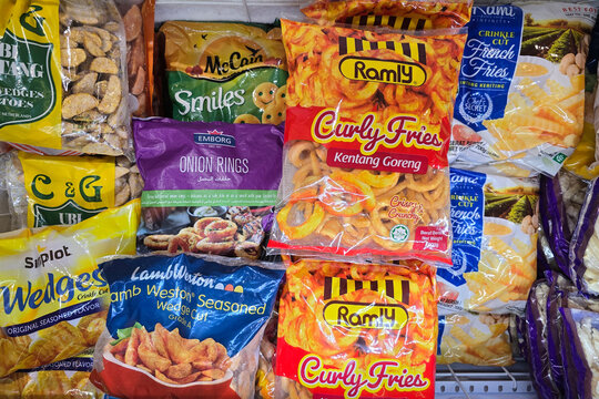 Penang, Malaysia - Mar 26, 2025: A variety of frozen snack products including curly fries, potato wedges, onion rings, and smiley fries on display in a supermarket freezer section.