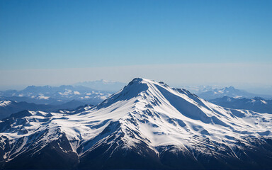 A majestic snow-covered mountain peak stands prominently against a clear blue sky. Distant mountain ranges are visible in the background, creating a scenic landscape of natural beauty.
