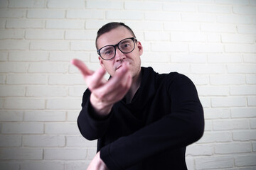 Man Dancing Joyfully in a Stylish Black Outfit With Glasses Against a Light Brick Wall Background