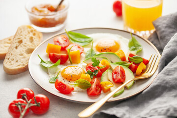 Healthy breakfast. Fried eggs and vegetables - cherry tomatoes, avocado slices, spinach leaves, sweet pepper and parsley in plate on the table