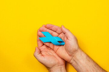 Courageous hands holding a blue ribbon for cancer awareness campaign